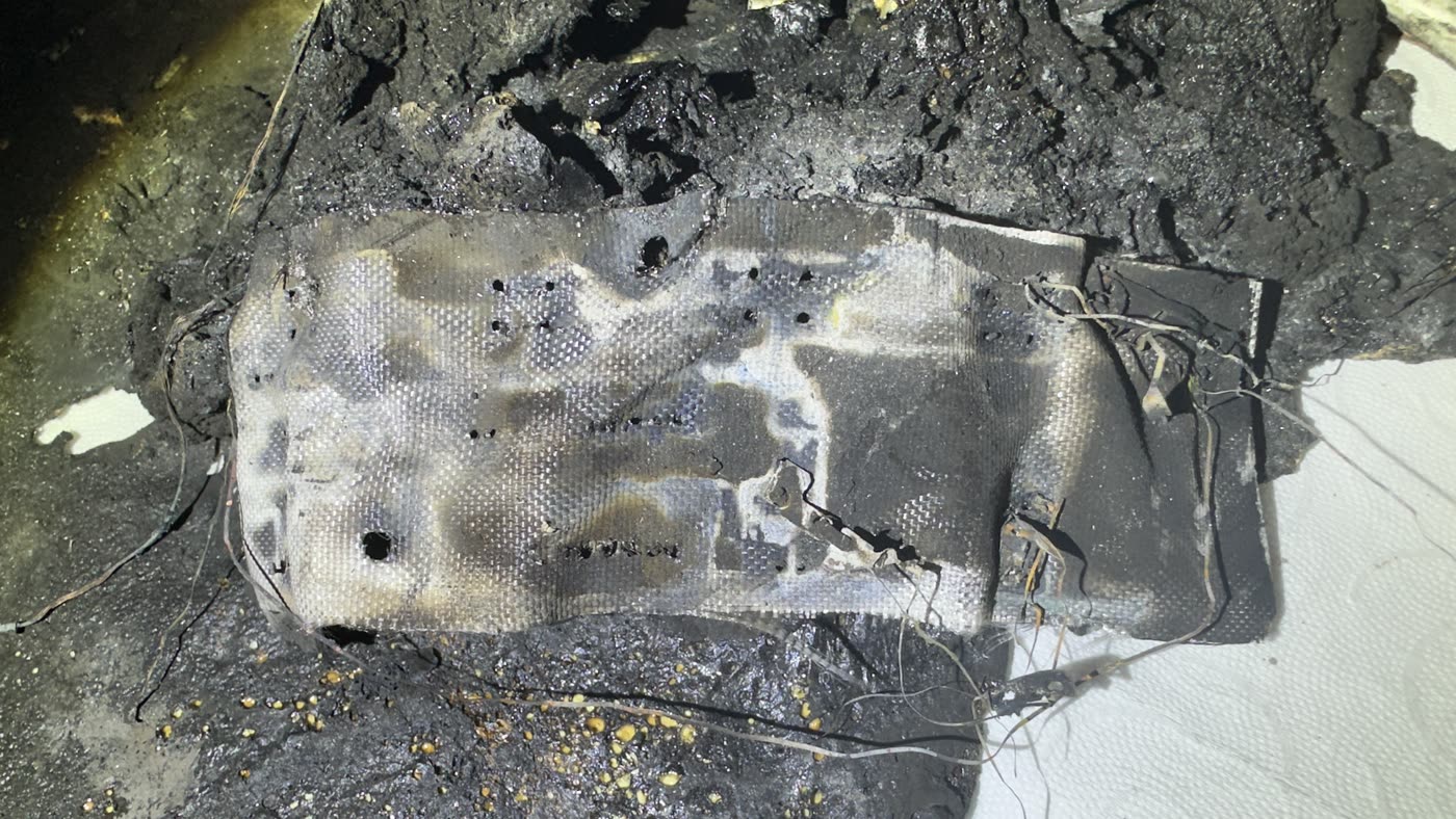 Charred remains of a display electronics circuit board, conductor tracks partly exposed, surrounding plastic completely burnt away.
