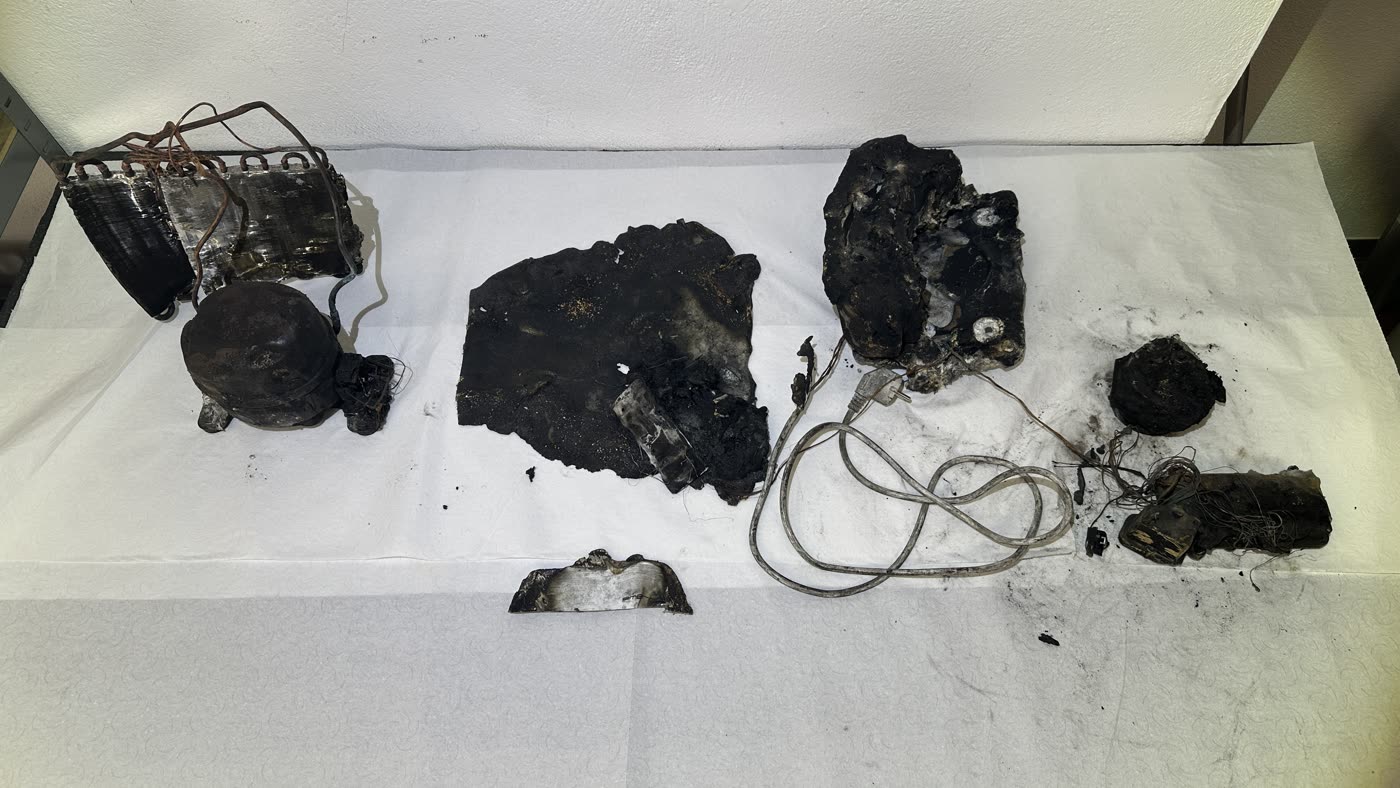 Fire debris from a dehumidifier laid out on a white cloth: heat exchanger, compressor, charred enclosure parts, mains lead with plug and remains of assemblies.