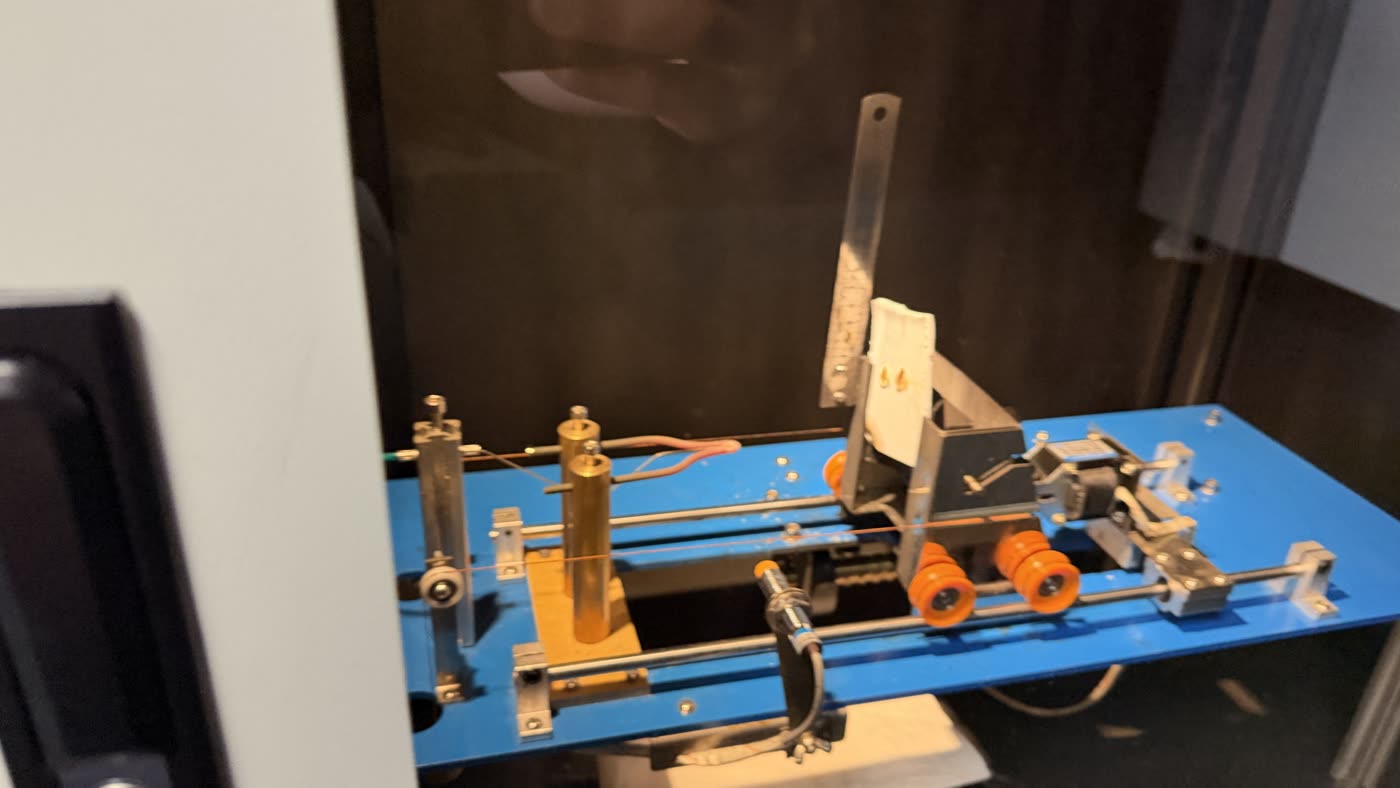 Glow-wire test at 750 degrees Celsius: the wire glows distinctly orange. Two holes from the preceding tests at 550 and 650 degrees are visible in the specimen.